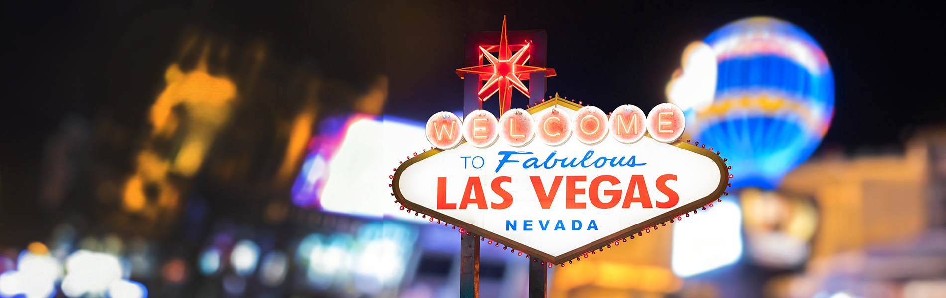 Las Vegas sign at night with lights and buildings in the background.