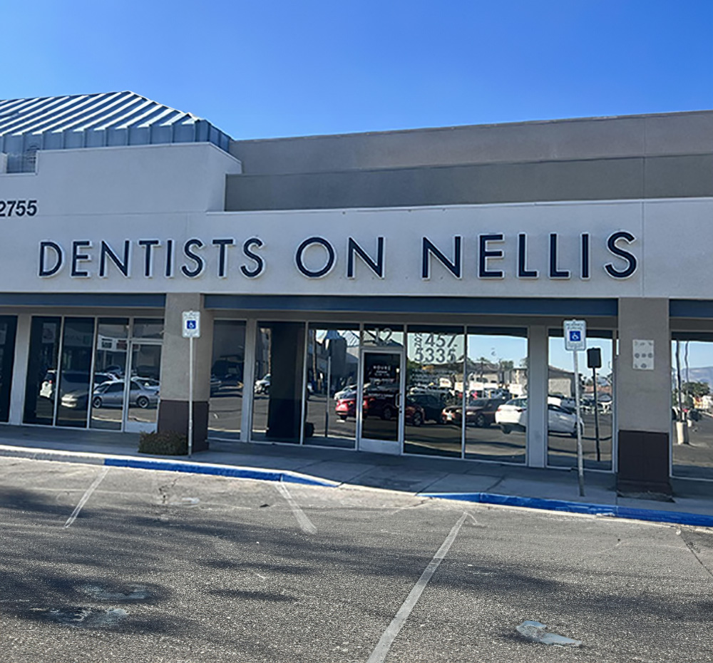 The image shows a sign for  Dentists on Nellis  in front of a building with a parking lot.
