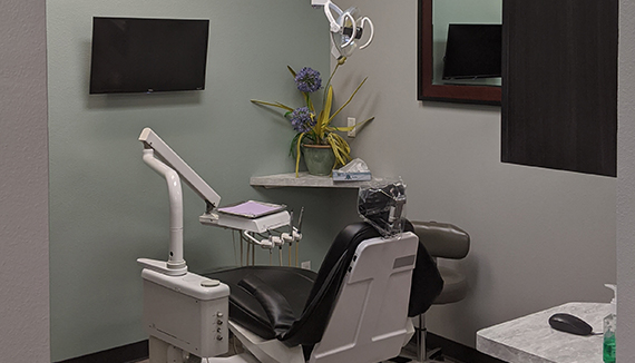 The image shows a dental office interior with a modern dental chair, a dental mirror, and various dental equipment.