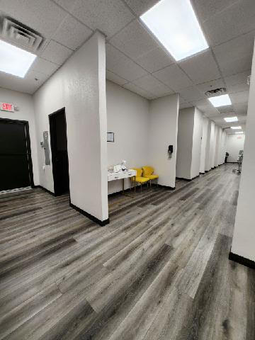 The image shows an interior view of a long, narrow room with a light-colored floor and walls, featuring laminate flooring and white ceiling tiles.