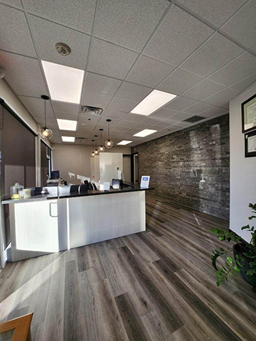 The image depicts an interior view of a modern office space with a reception area, featuring a clean and minimalist design with a large window allowing natural light to enter.