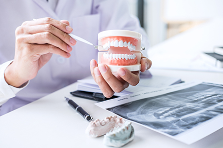 A dental professional examining a model mouth with dental tools, surrounded by medical equipment and a collection of dental models.
