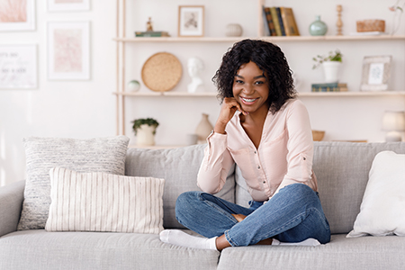 A young woman with a smile, seated on a couch in a cozy living room setting.