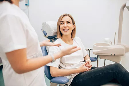 Woman in a dental chair receiving dental care with a smiling hygienist standing behind her.