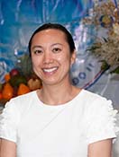 The image shows a smiling woman standing in front of a backdrop with a floral pattern, which suggests she may be at an event or ceremony.